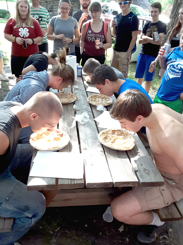 Teenagers with arms behind their backs eating pie at a contest