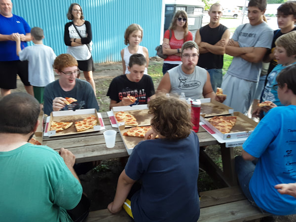 Group of people sitting at a table eating Pizza at an eating contest